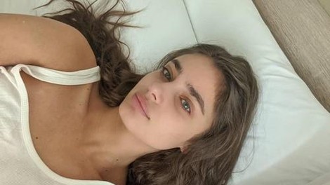 Mlada ženska leži na postelji in dela selfie.